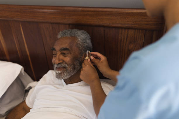High angle view of a young African American female doctor fitting a senior African American man with hearing aid in bedroom at home
